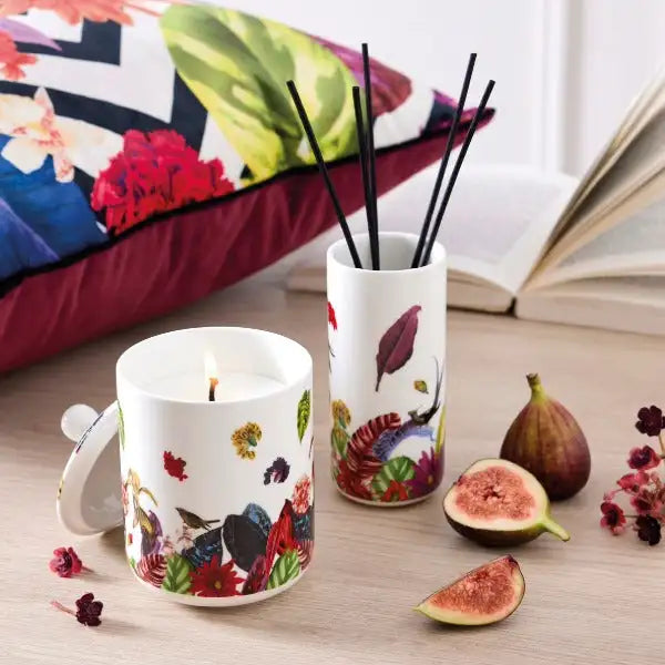 Porte-bougies en céramique blanche avec une flamme allumée, orné d'illustrations botaniques vibrantes d'oiseaux et de fleurs en rouges, verts et violets.